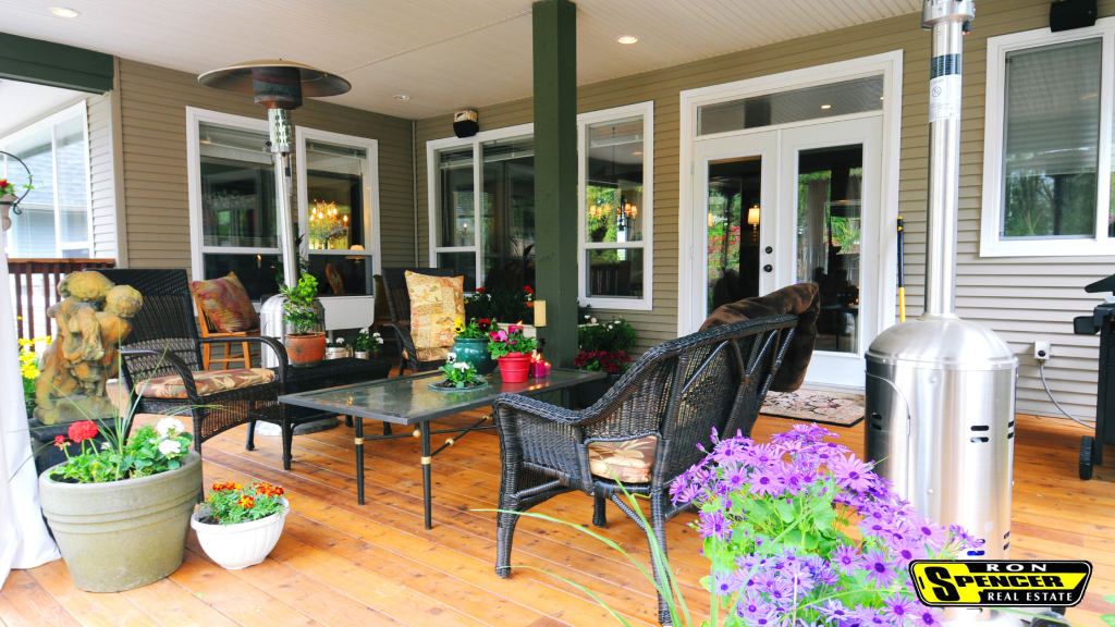 Outdoor covered patio with hardwood floors, black pillars, white trim, black patio chairs and table with colorful potted flowers sititng around. 