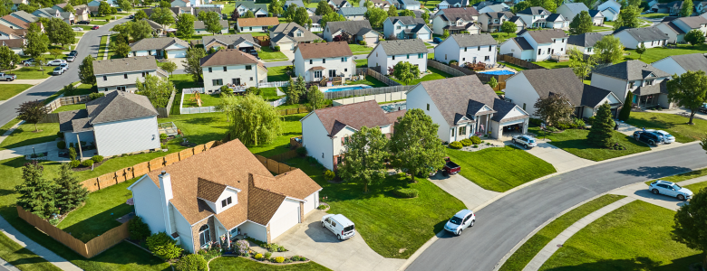 Aerial view of a neighborhood with several nice looking homes and green grass lawns on a curved road with cars in the driveways.