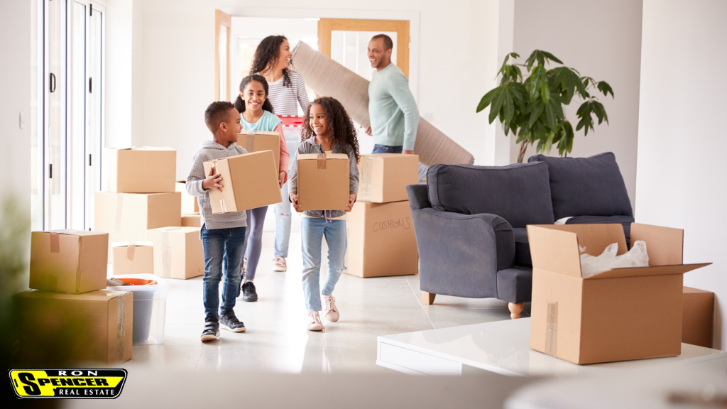 African American Family, a mom, dad, two girls and one boy carrying moving boxes and smiling at each other