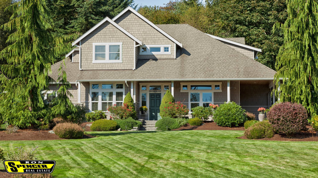 Large two story home with beige siding and white trim and a very green manicured front lawn with green bushes and colorful trees