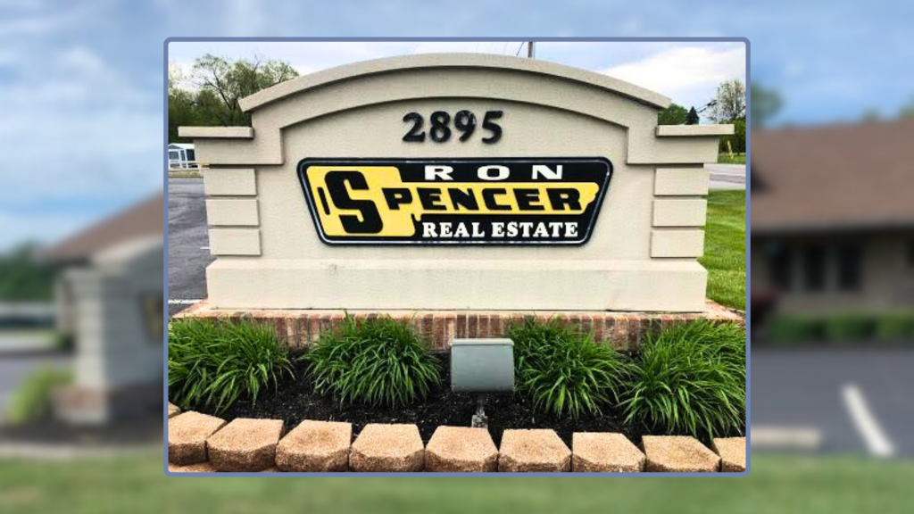 Ron Spencer Real Estate Signage in the parking log of the Ron Spencer Real Estate office building wiht green plants and landscaping and red bricks 