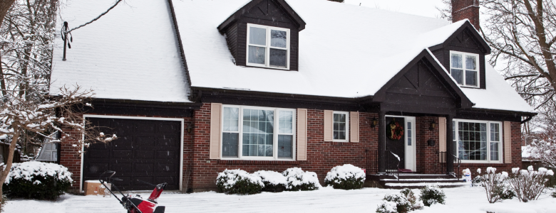 Brick home covered in a light dusting of snow with a red snowblower in the driveway