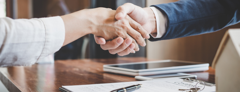 two caucasian arms shaking hands at a wood desk over paperwork