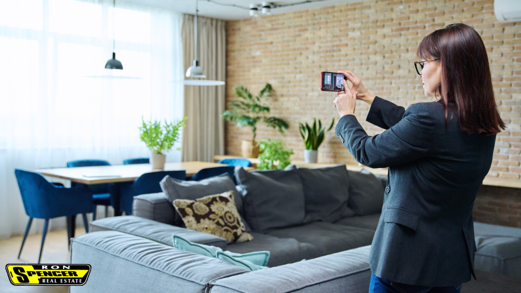 caucasian woman standing in a living room taking a picture of the room with her cellphone