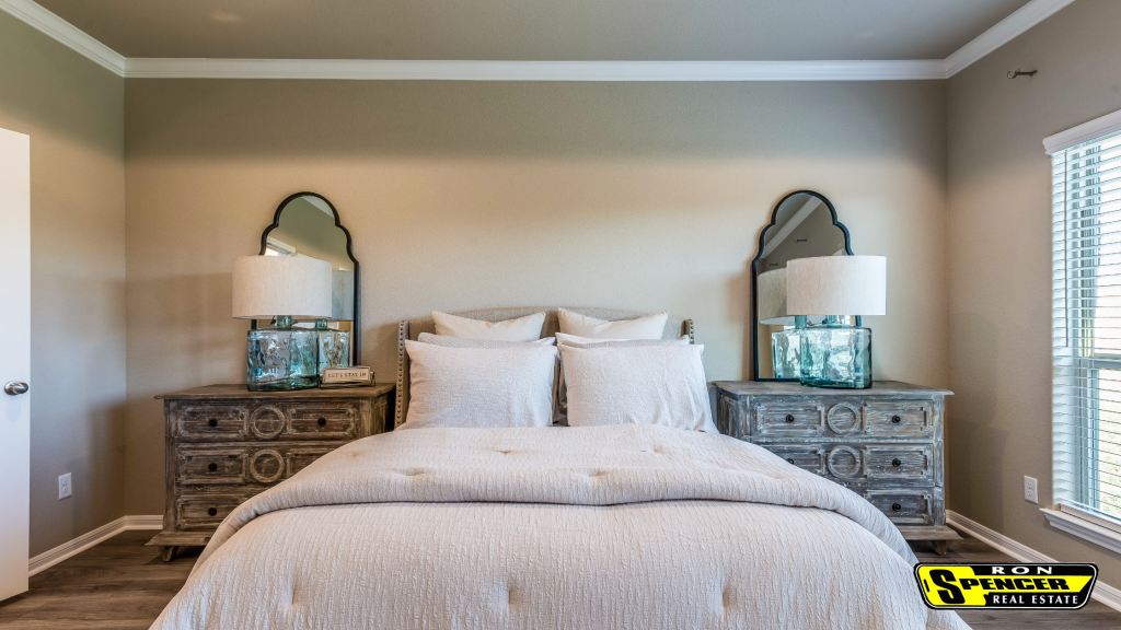 Staged bedroom in a home for sale white bedding matching lamps and mirrors and side tables with white blinds on the window and beige walls