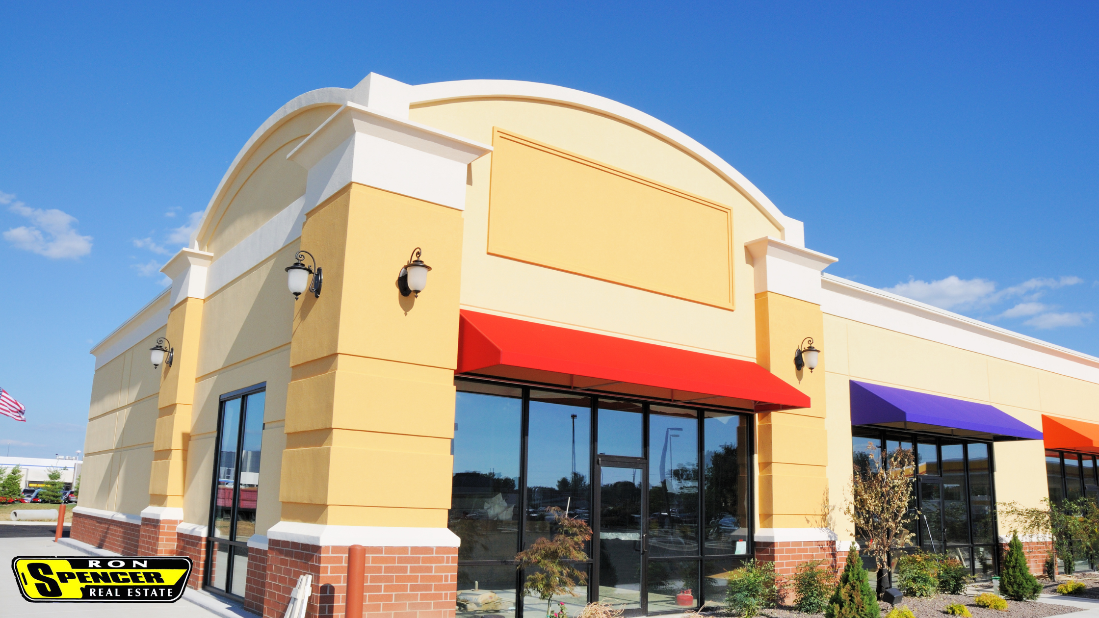 Beige commercial building for sale with red awning and bright blue sky glass windows and door with black trim to highlight commercial real estate