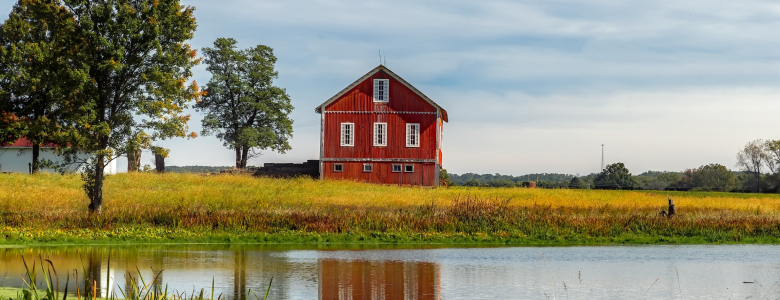 Farmland with a pond overlooking a red barn and blue skies