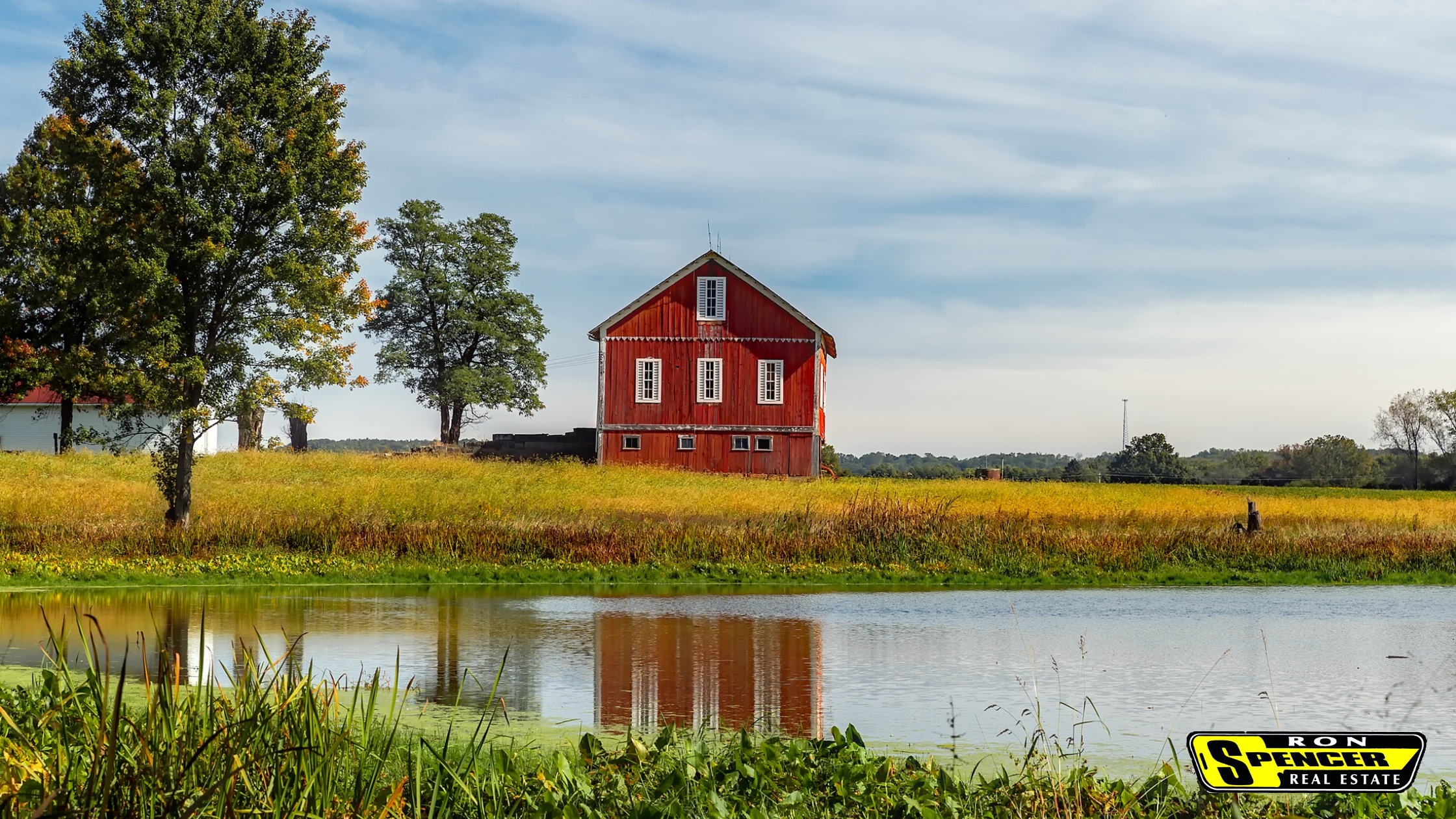 Farmland with a pond overlooking a red barn and blue skies