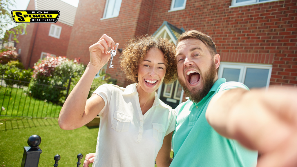 Photo of a man and woman taking a selfie in front of a new house smiling and holding up a house key