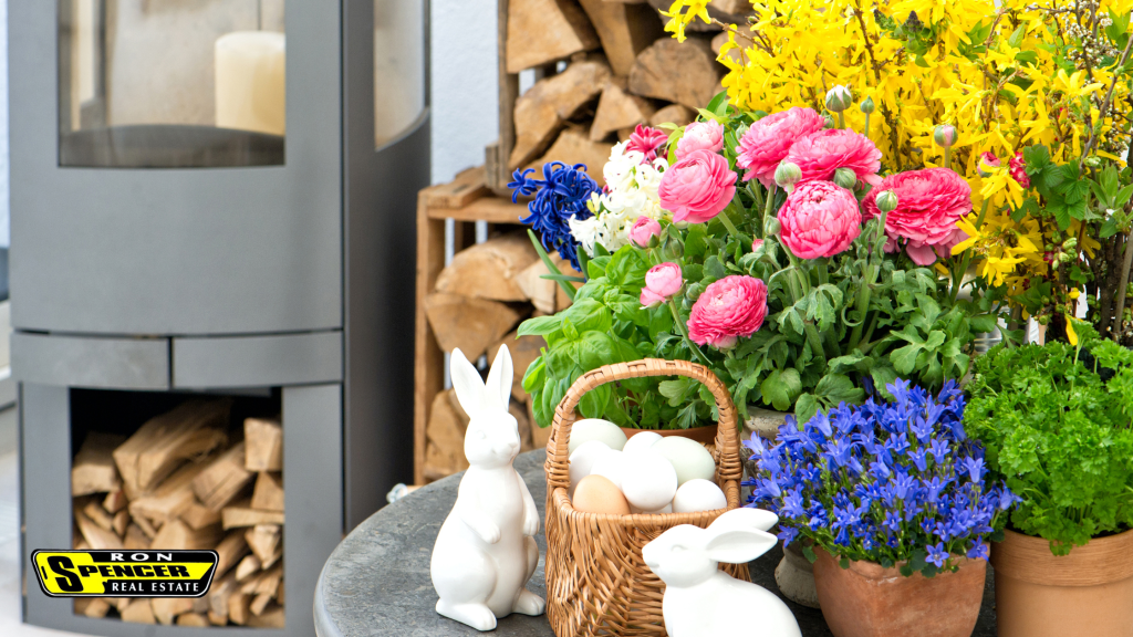 Front porch of a home with gray siding, bright pink and yellow and purple spring flowers and white ceramic bunnies in a basket