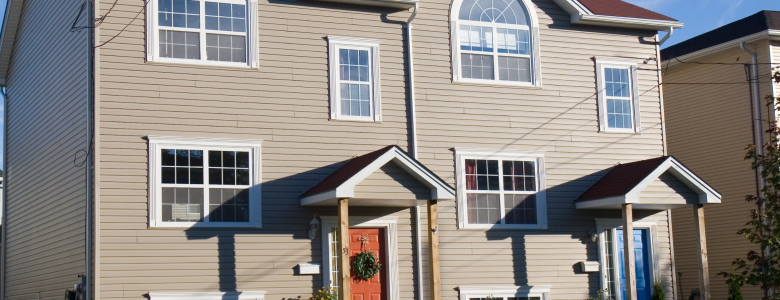Tan tiled home with red shingle roof and red front door with the sun shining on it and blue skies