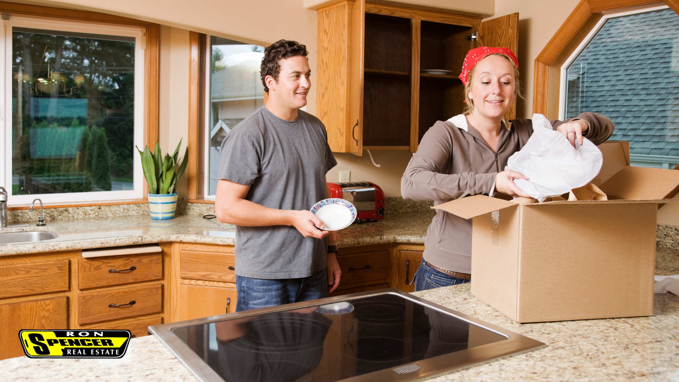 a caucasian man and woman in gray shirts standing in a kitchen unpacking boxes with plates wrapped in bubble wrap