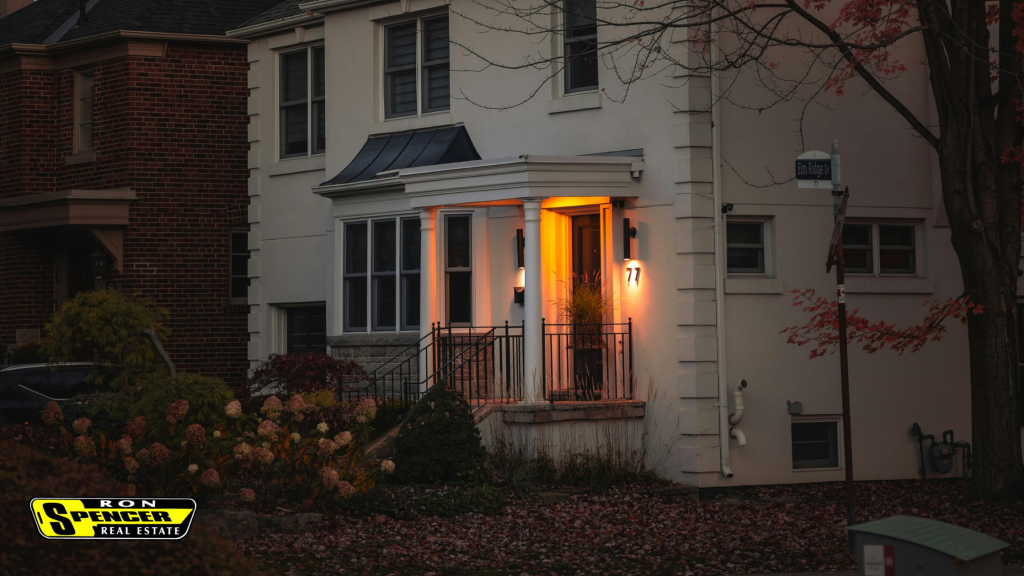 Front facade of a white house with a red door pictures in the evening after dark with 2 porch lights illuminating the front steps