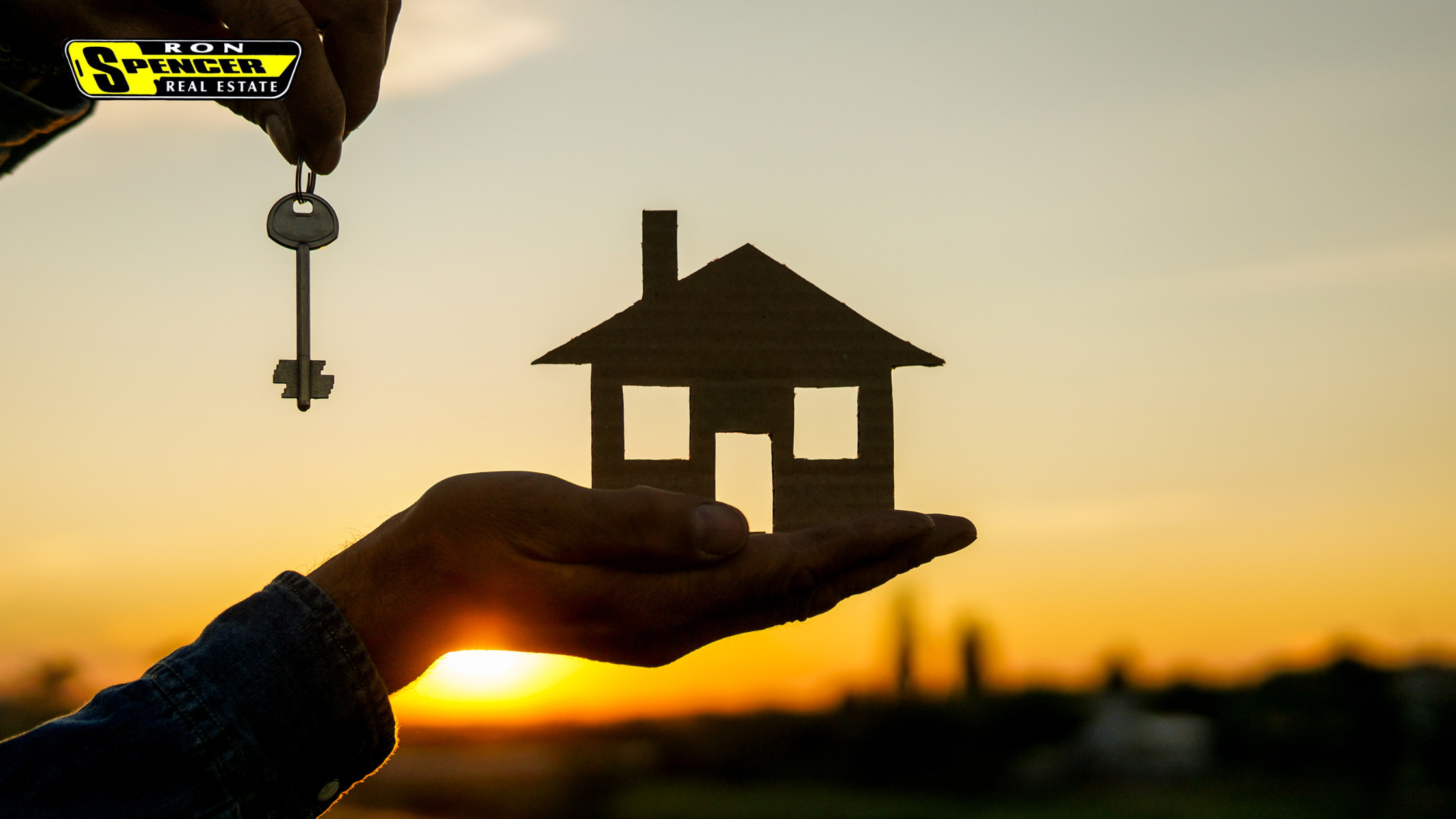 hand holding a cutout of a house in front of a sunset and the other hand holding a key