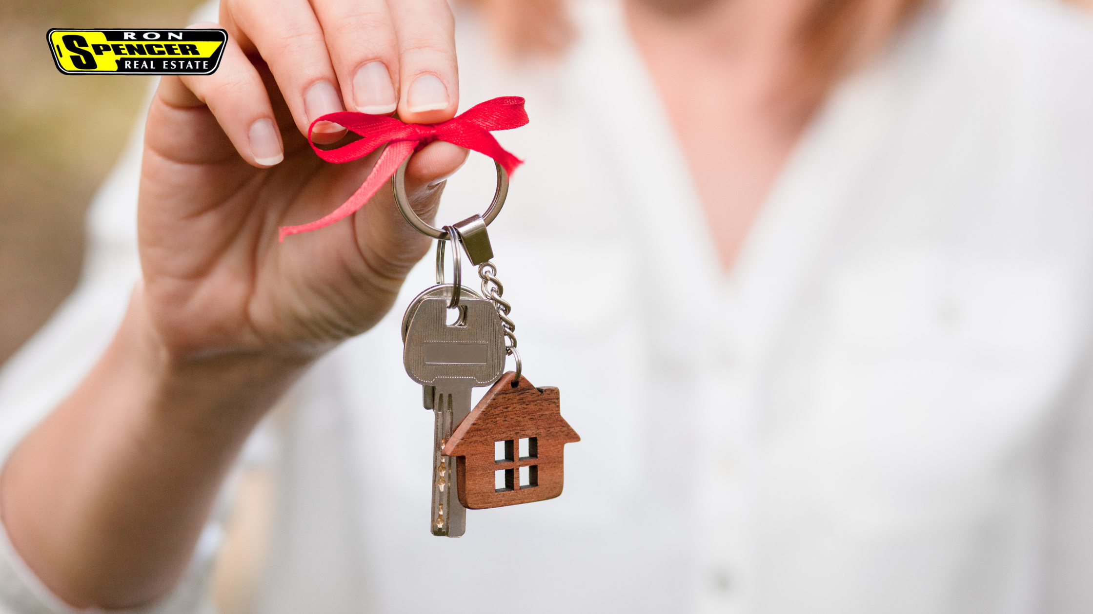 caucasian hand holding a set of house keys tied with a red ribbon