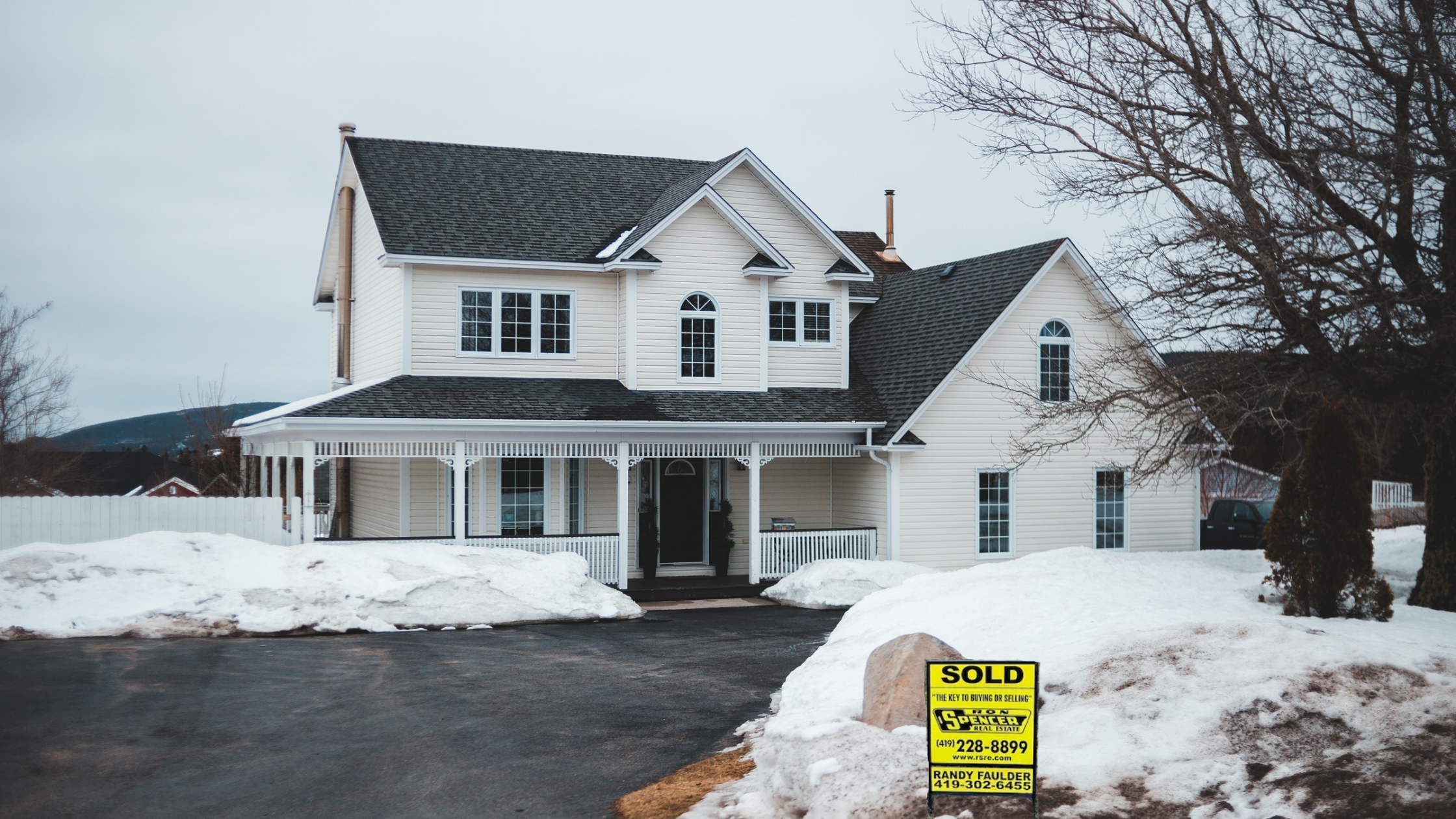 two story white house with large driveway, snow on the ground, a ron spencer real estate SOLD sign in the yard